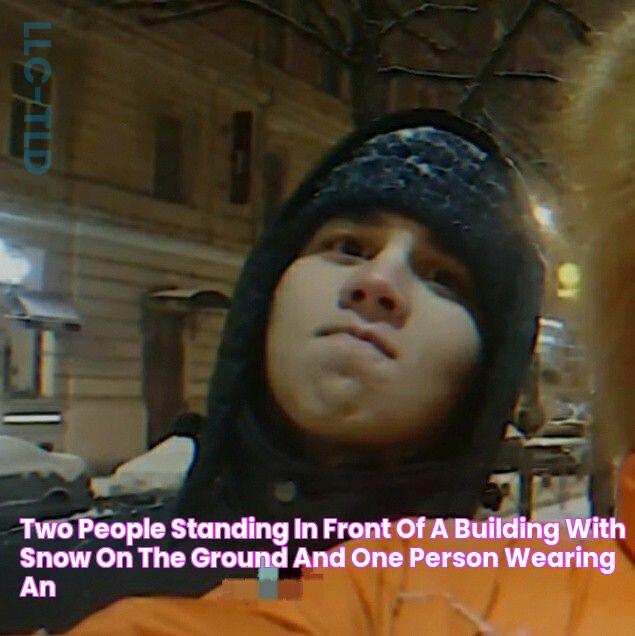 two people standing in front of a building with snow on the ground and one person wearing an